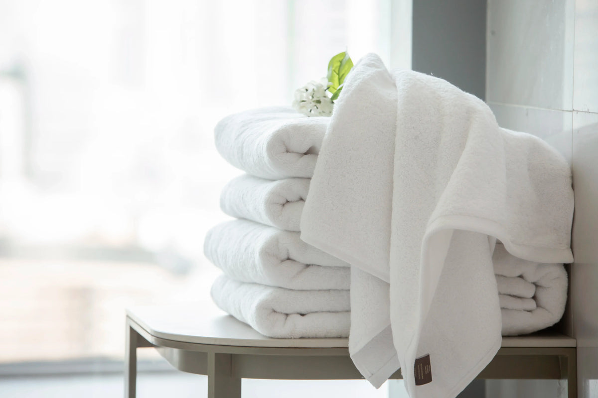 Maison 1952 Retreat Collection: 650 GSM white cotton towels folded and draped in a bright bathroom