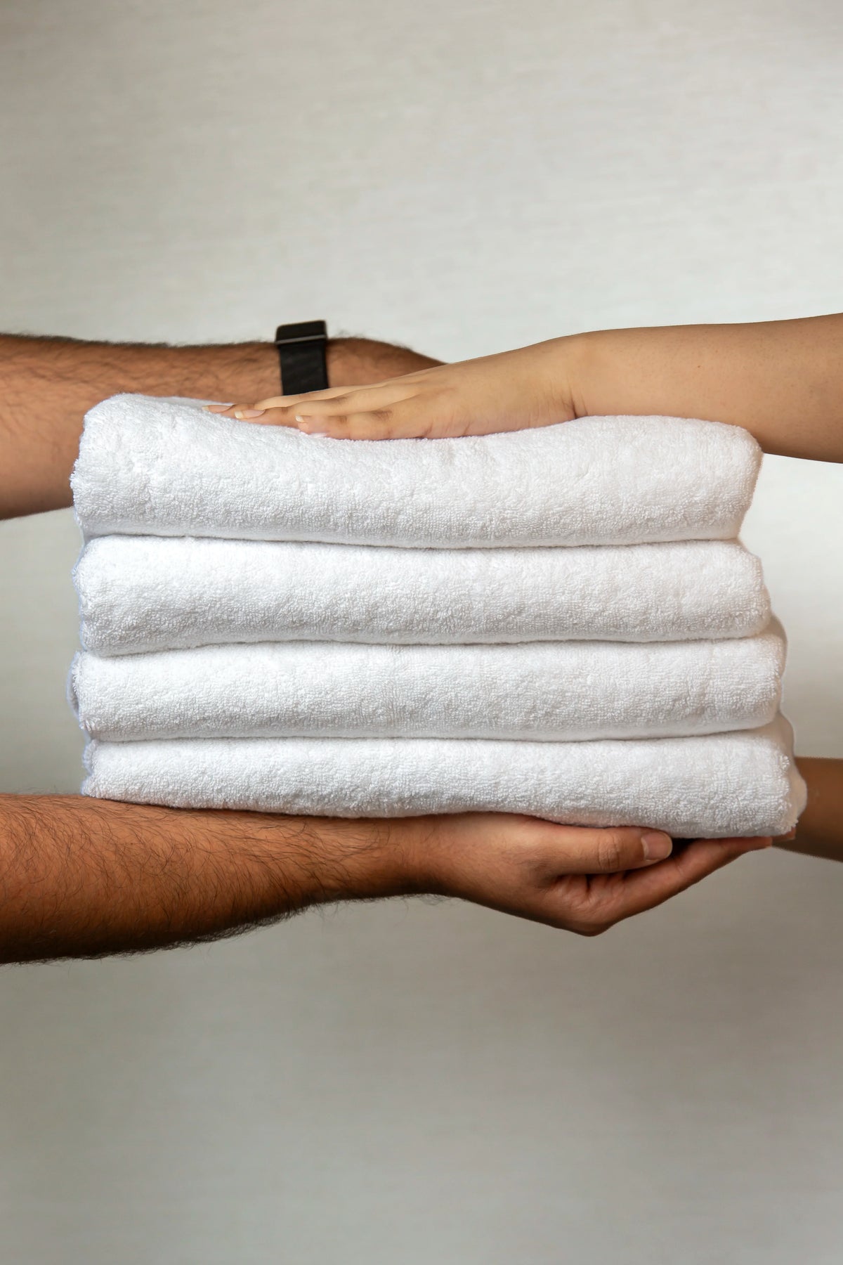 Two pairs of hands holding a stack of four folded Retreat white cotton towels