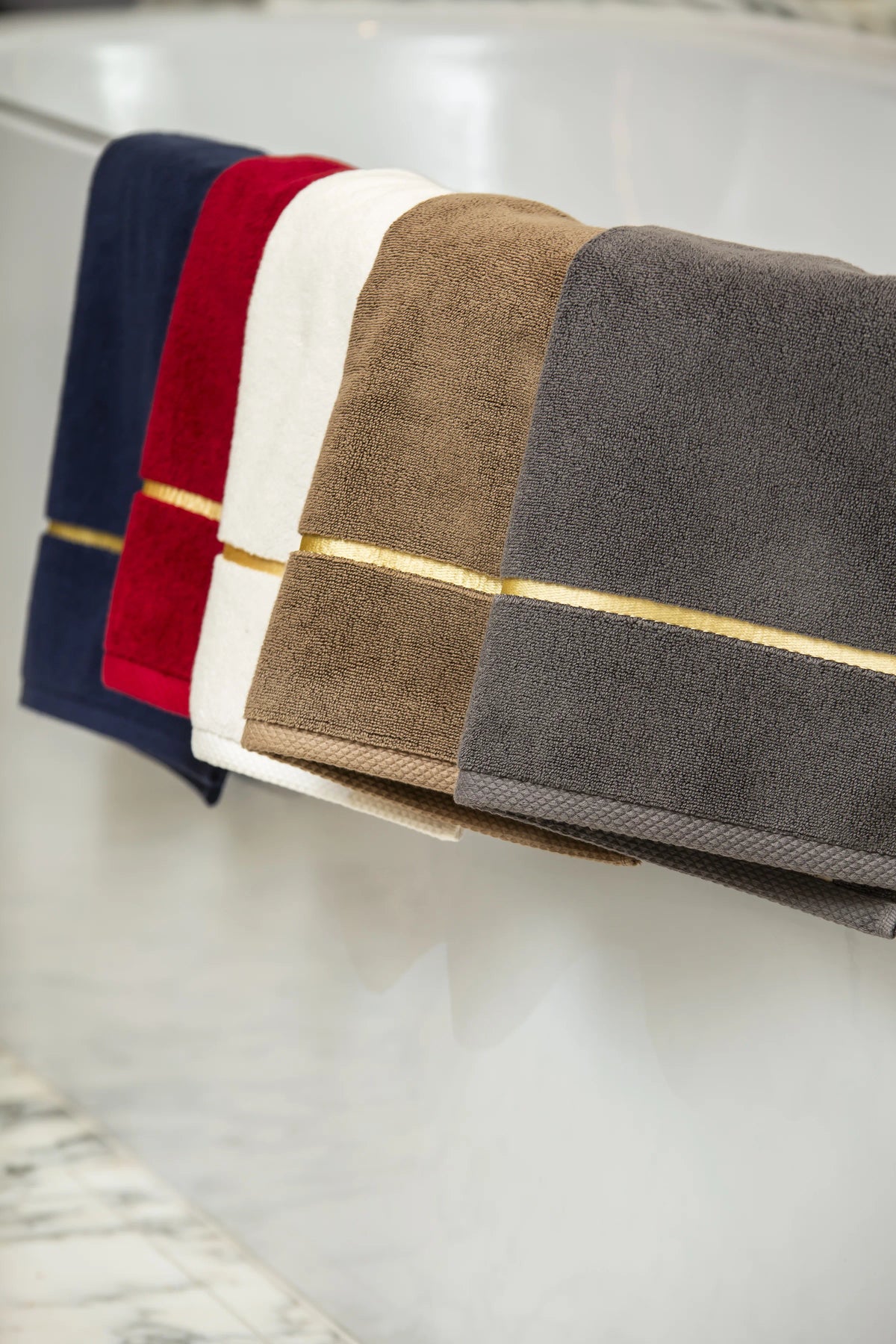 Five Chateau Turkish cotton bath mats in navy blue, maroon, white, brown and grey draped over a bathtub edge 