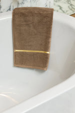 Brown Chateau Turkish cotton towel draped over the edge of a bathtub 