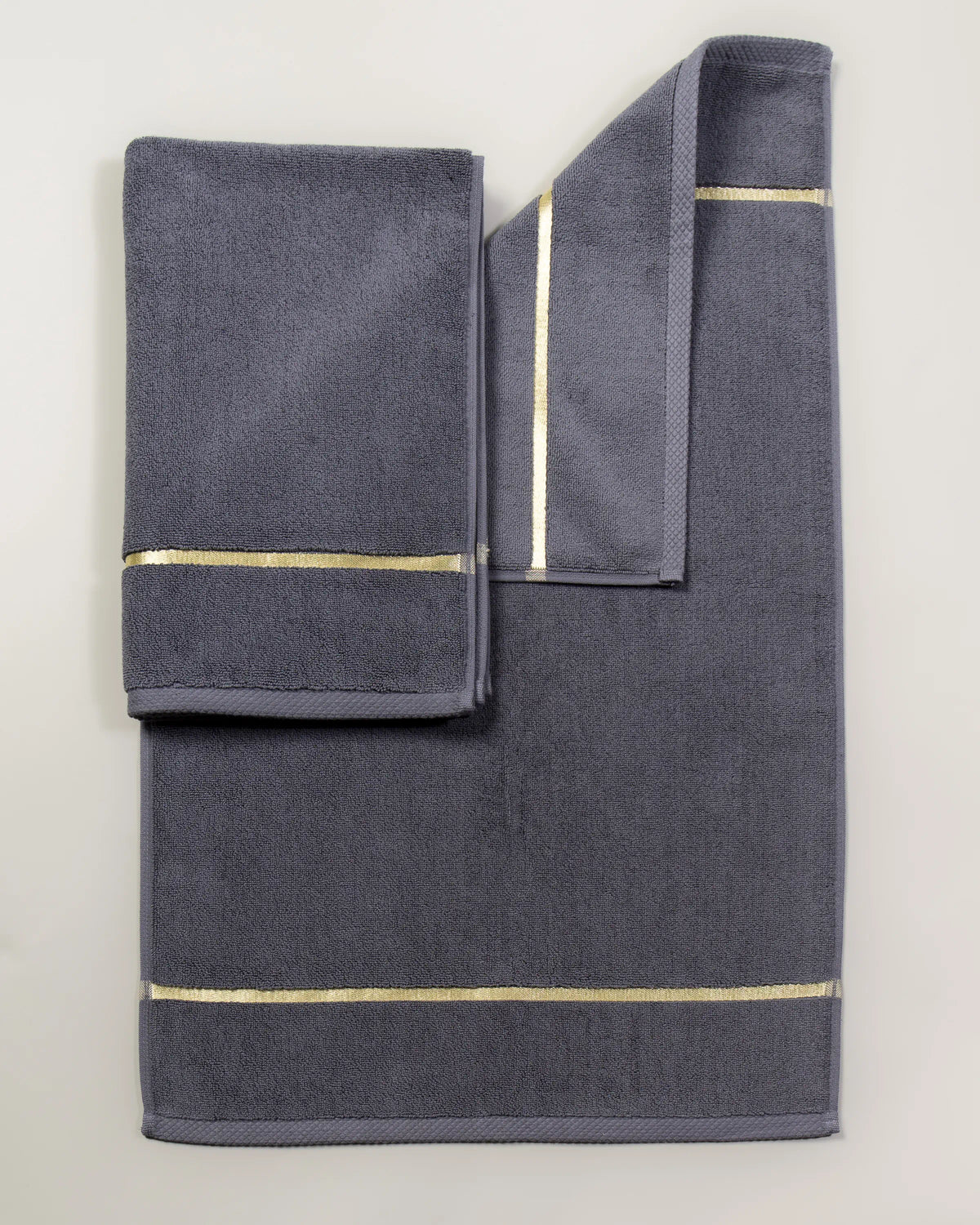 Grey Chateau Turkish cotton bath mat, laid flat on a studio backdrop with two small towels on top 