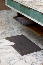 Grey Chateau Turkish cotton bath mat, on a marble bathroom floor with white slippers 