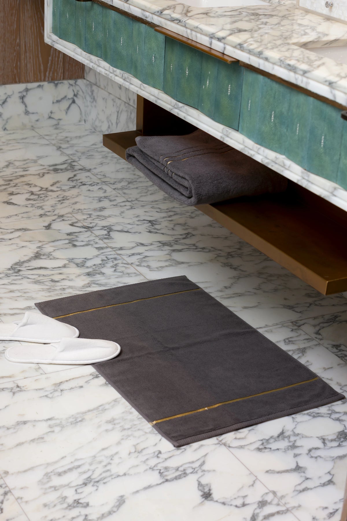 Grey Chateau Turkish cotton bath mat, on a marble bathroom floor with white slippers 