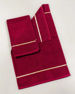 Maroon Chateau Turkish cotton bath mat, laid flat on a studio backdrop with two small towels on top 