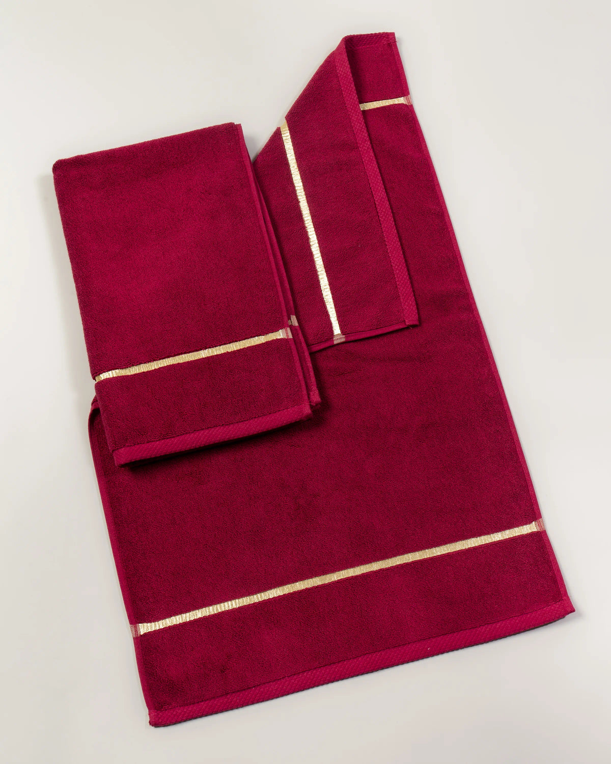 Maroon Chateau Turkish cotton bath mat, laid flat on a studio backdrop with two small towels on top 
