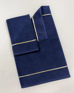 Navy Blue Chateau Turkish cotton bath mat, laid flat on a studio backdrop with two small towels on top 