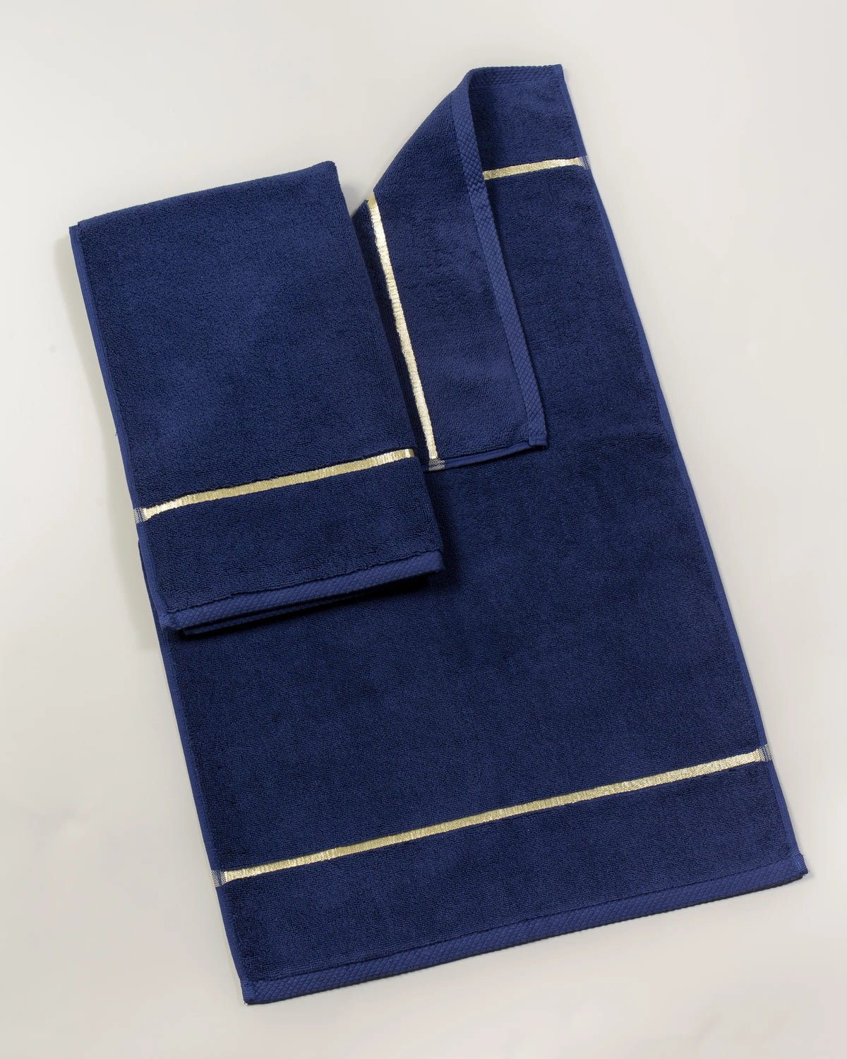 Navy Blue Chateau Turkish cotton bath mat, laid flat on a studio backdrop with two small towels on top 