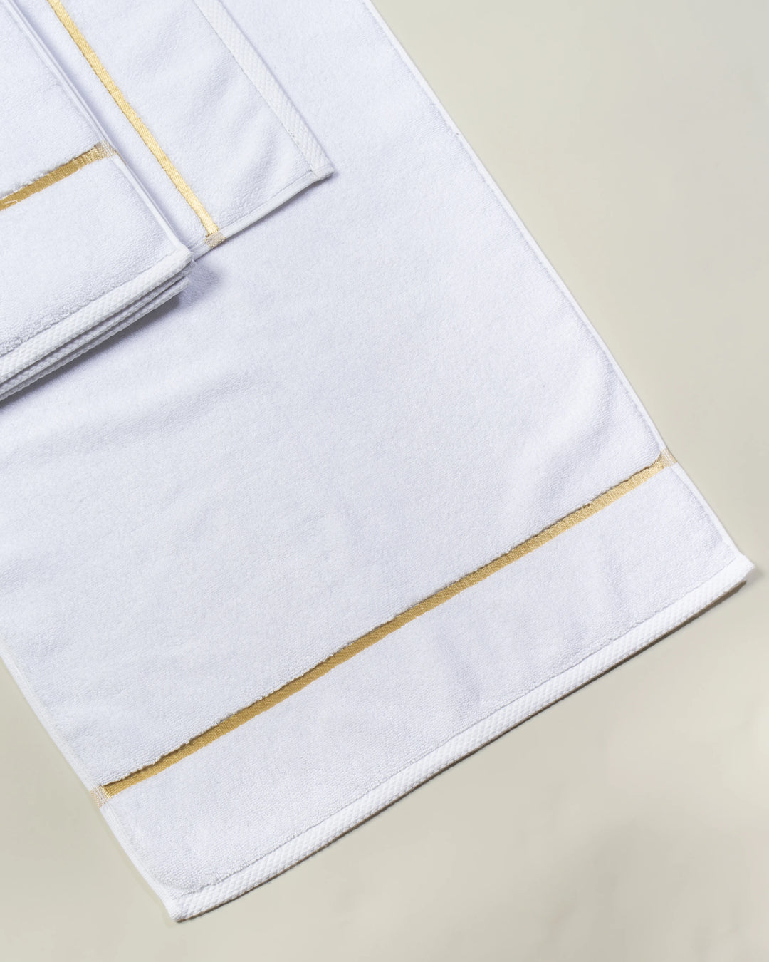 White Chateau Turkish cotton bath mat, laid flat on a studio backdrop with two small towels on top 
