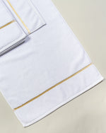 White Chateau Turkish cotton bath mat, laid flat on a studio backdrop with two small towels on top 