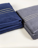 Navy blue and grey Chateau Turkish cotton bath sheets folded side by side, gold border lines on each 