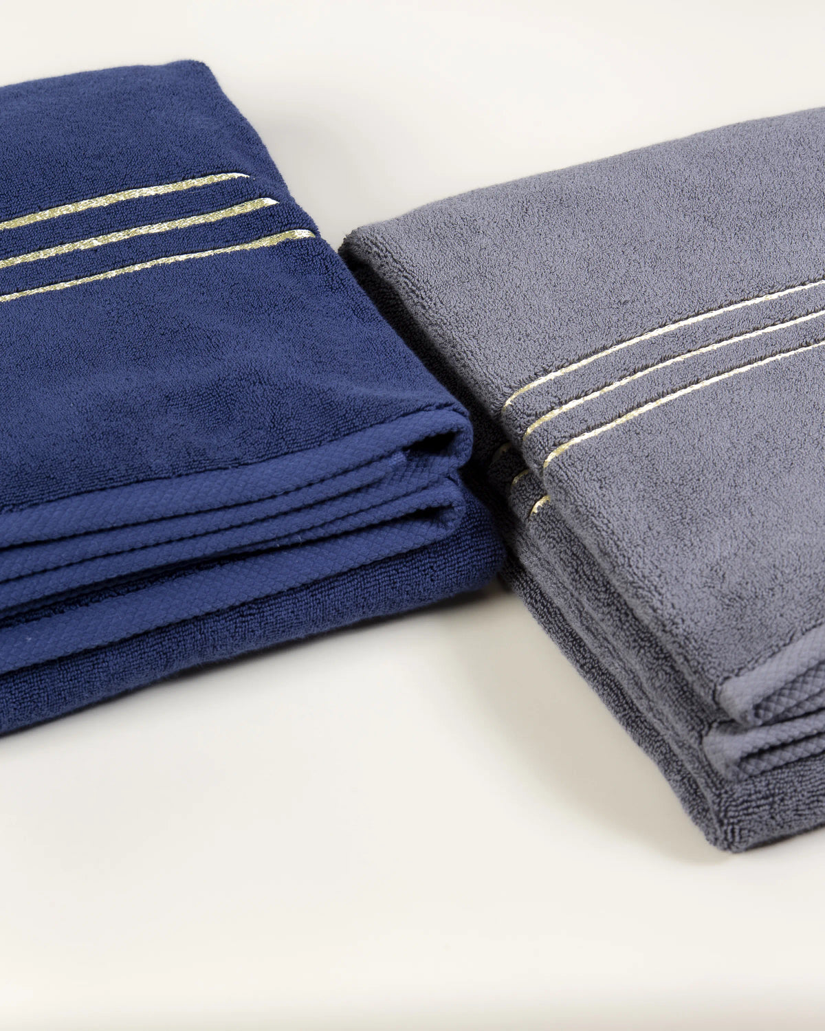 Navy blue and grey Chateau Turkish cotton bath sheets folded side by side, gold border lines on each 