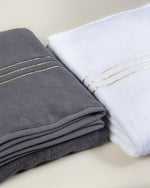Grey and white Chateau Turkish cotton bath sheets folded side by side, gold border lines on each 
