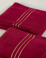 Toalla de baño Chateau de algodón turco, color granate, dos piezas dobladas, primer plano de los bordes dobby dorados 