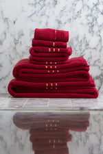 Toallas de baño, de manos y faciales Chateau de algodón turco, color granate, apiladas por tamaños sobre mármol 