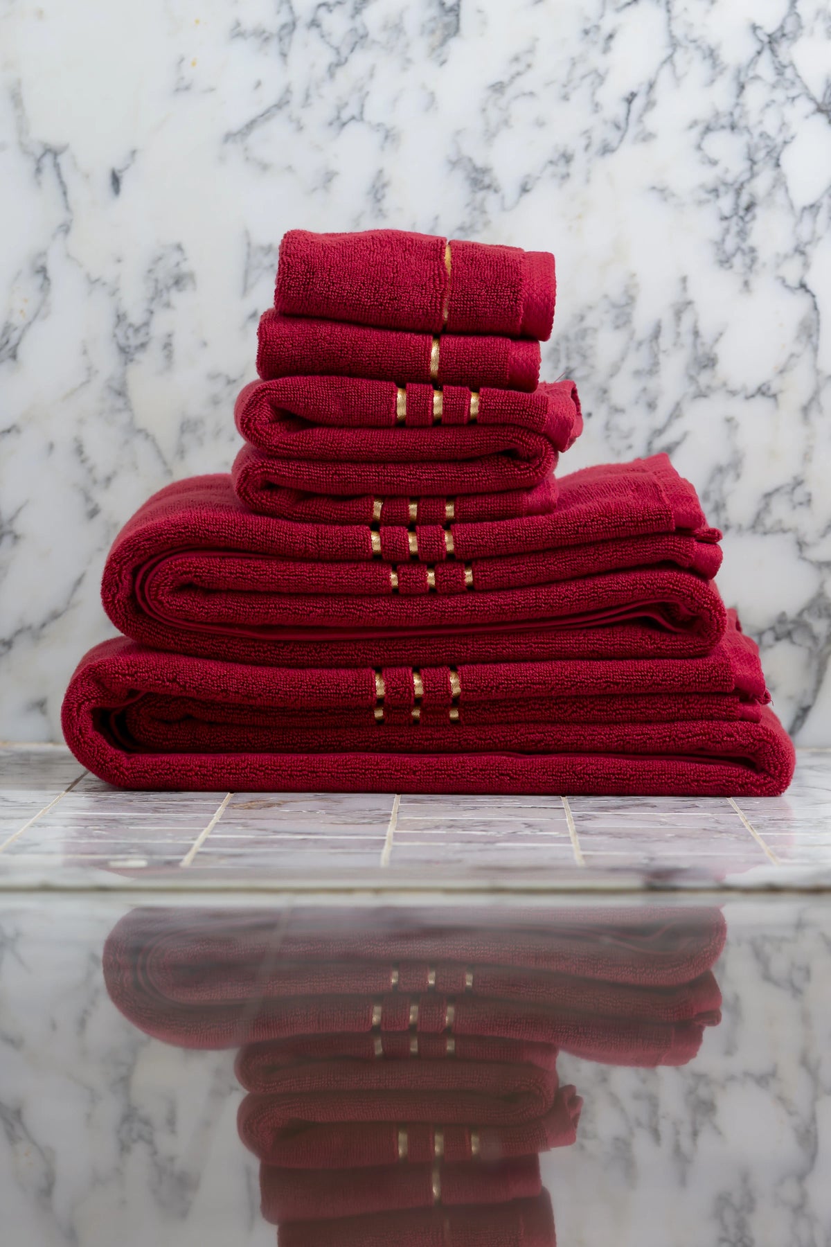 Toallas de baño, de manos y faciales Chateau de algodón turco, color granate, apiladas por tamaños sobre mármol 