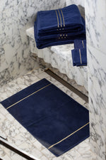 Toallas de baño Chateau de algodón turco, color azul marino, apiladas sobre una repisa de mármol encima de una alfombra de baño azul marino 