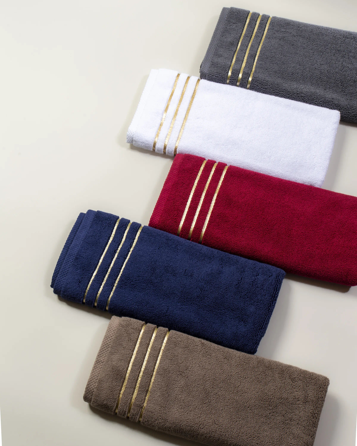 Cinque asciugamani Chateau piegati in cotone turco, colori grigio, bianco, bordeaux, blu navy e marrone, disposti uno accanto all'altro