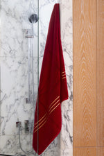 Set Chateau Essentials, colore bordeaux – telo da bagno appeso in una doccia di marmo e vetro 