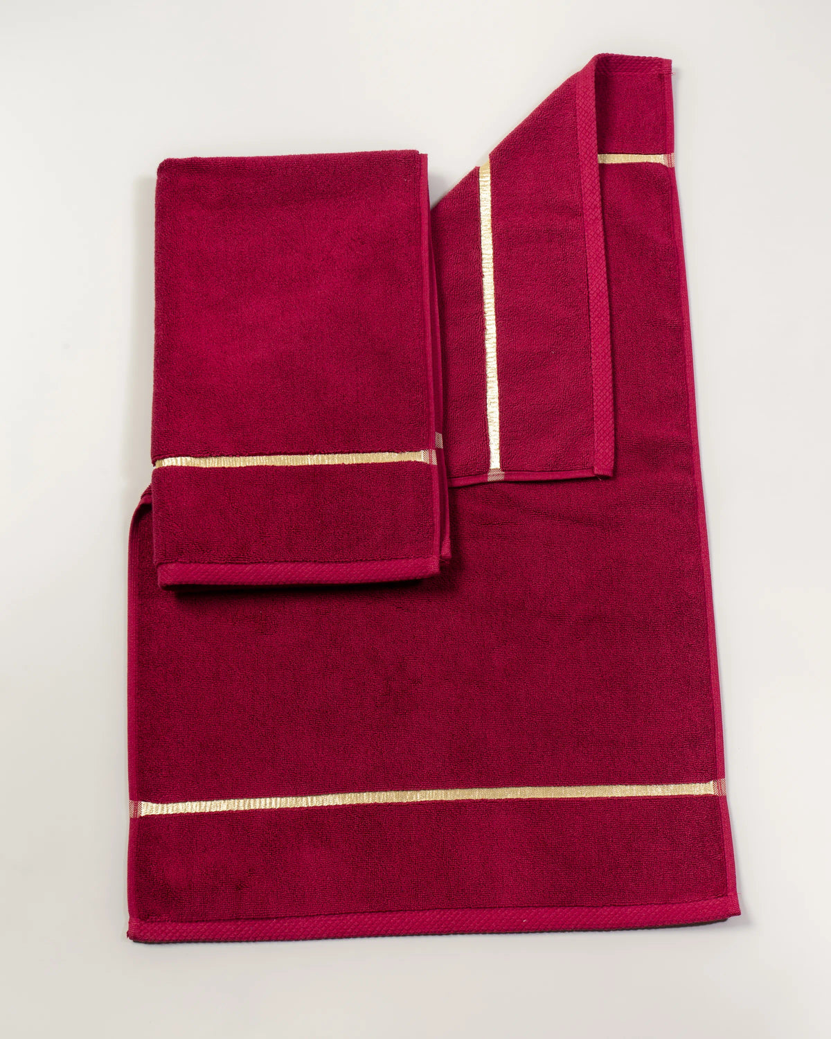Set Chateau Essentials, colore bordeaux – tappeto da bagno steso in piano con due asciugamani sopra 