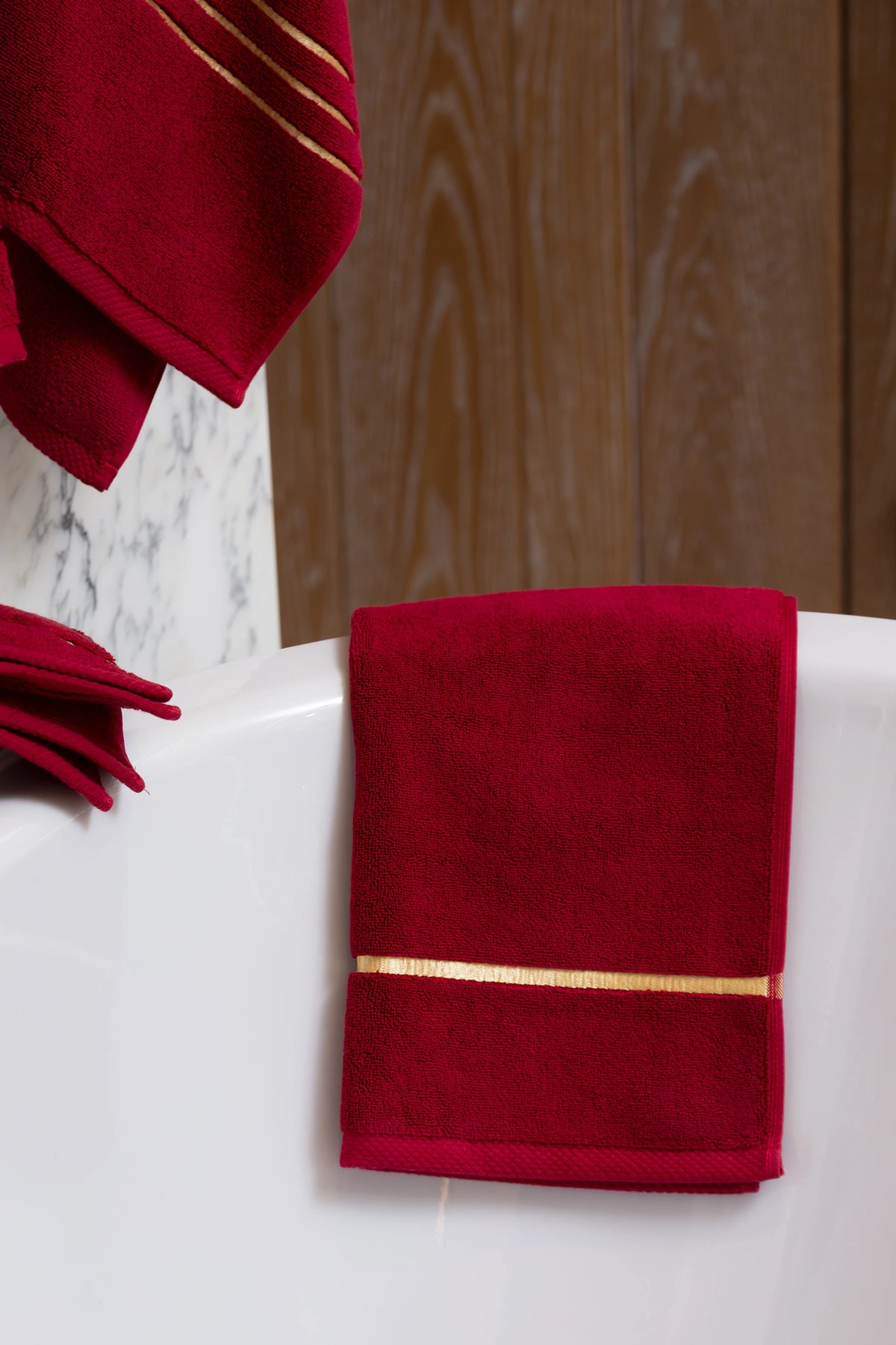 Set Chateau Essentials, colore bordeaux – asciugamano adagiato su una vasca con un telo da bagno appeso dietro 