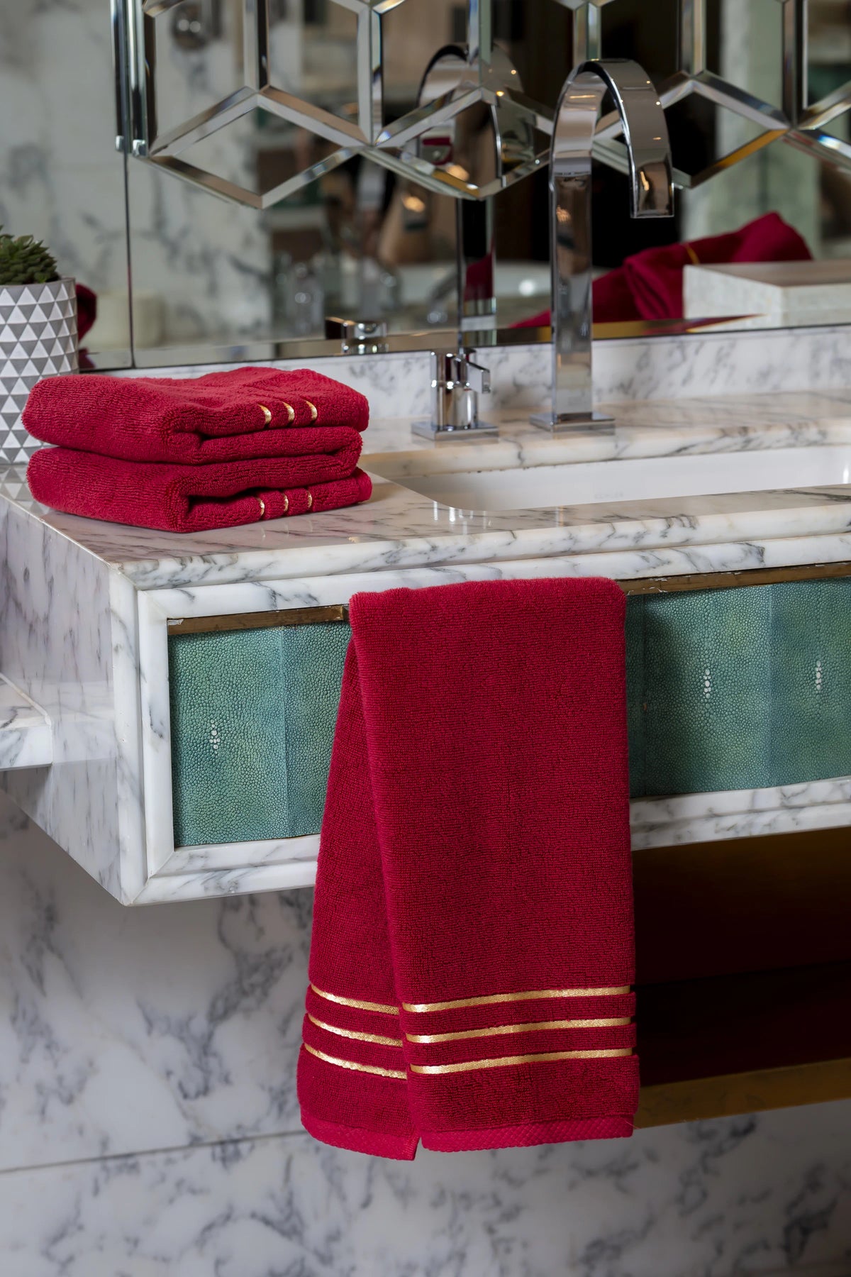 Set Chateau Essentials, colore bordeaux – asciugamano appeso a un mobile lavabo in marmo con una pila piegata sopra 