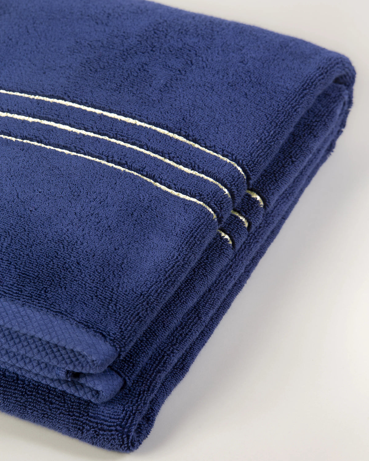 Set Chateau Essentials, colore blu navy – primo piano delle tre righe dorate sul telo da bagno piegato 
