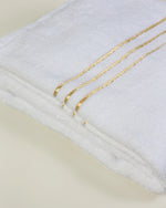 Set Chateau Essentials, colore bianco – primo piano delle tre righe dorate sul telo da bagno piegato 