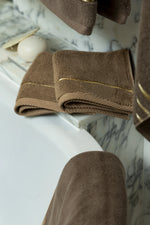 Brown Chateau Turkish cotton face towel, draped over the edge of a bathtub 
