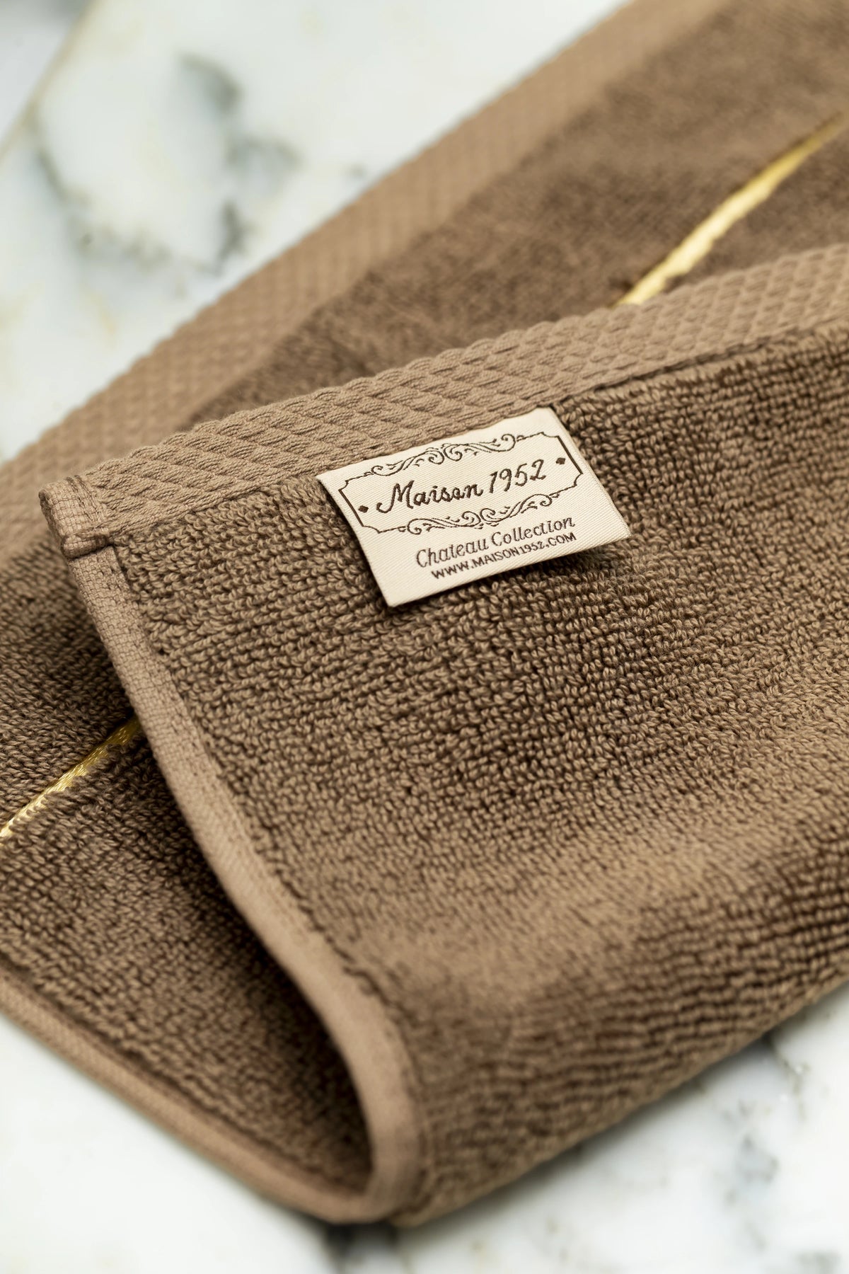 Maison 1952 Chateau Collection woven label on a brown Turkish cotton face towel 