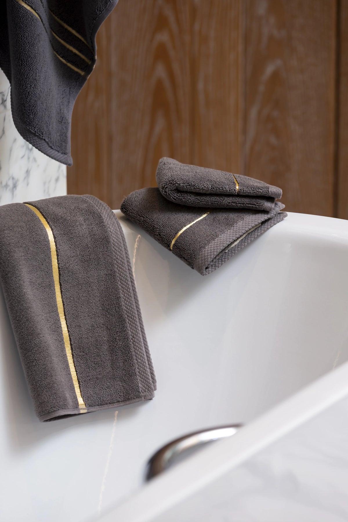 Grey Chateau Turkish cotton face towel, draped over the edge of a bathtub 