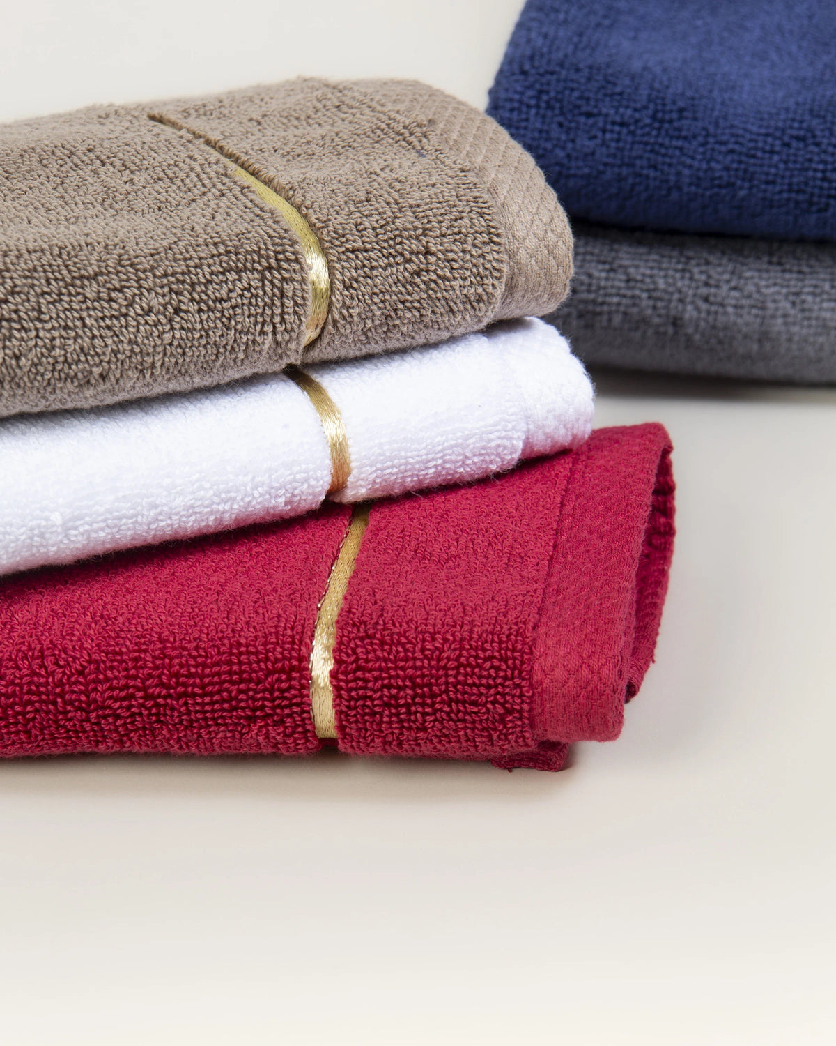 Brown, white and maroon Chateau Turkish cotton face towels stacked together, with navy blue and grey behind 