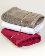 Brown, white and maroon Chateau Turkish cotton face towels stacked together, each with a single gold border line 