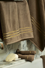 Brown Chateau Turkish cotton hand towel, hanging beside a marble bathtub 