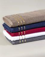 Stack of five Chateau Turkish cotton hand towels in brown, navy blue, maroon, white and grey with three gold border lines 