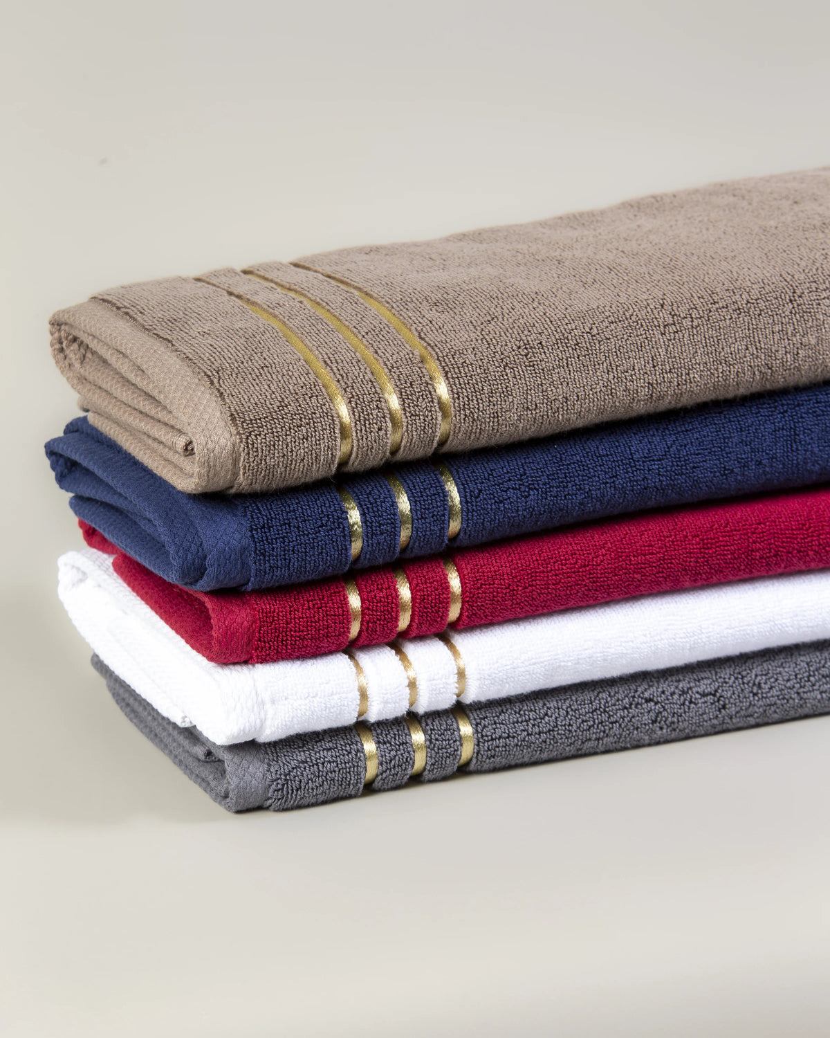 Stack of five Chateau Turkish cotton hand towels in brown, navy blue, maroon, white and grey with three gold border lines 