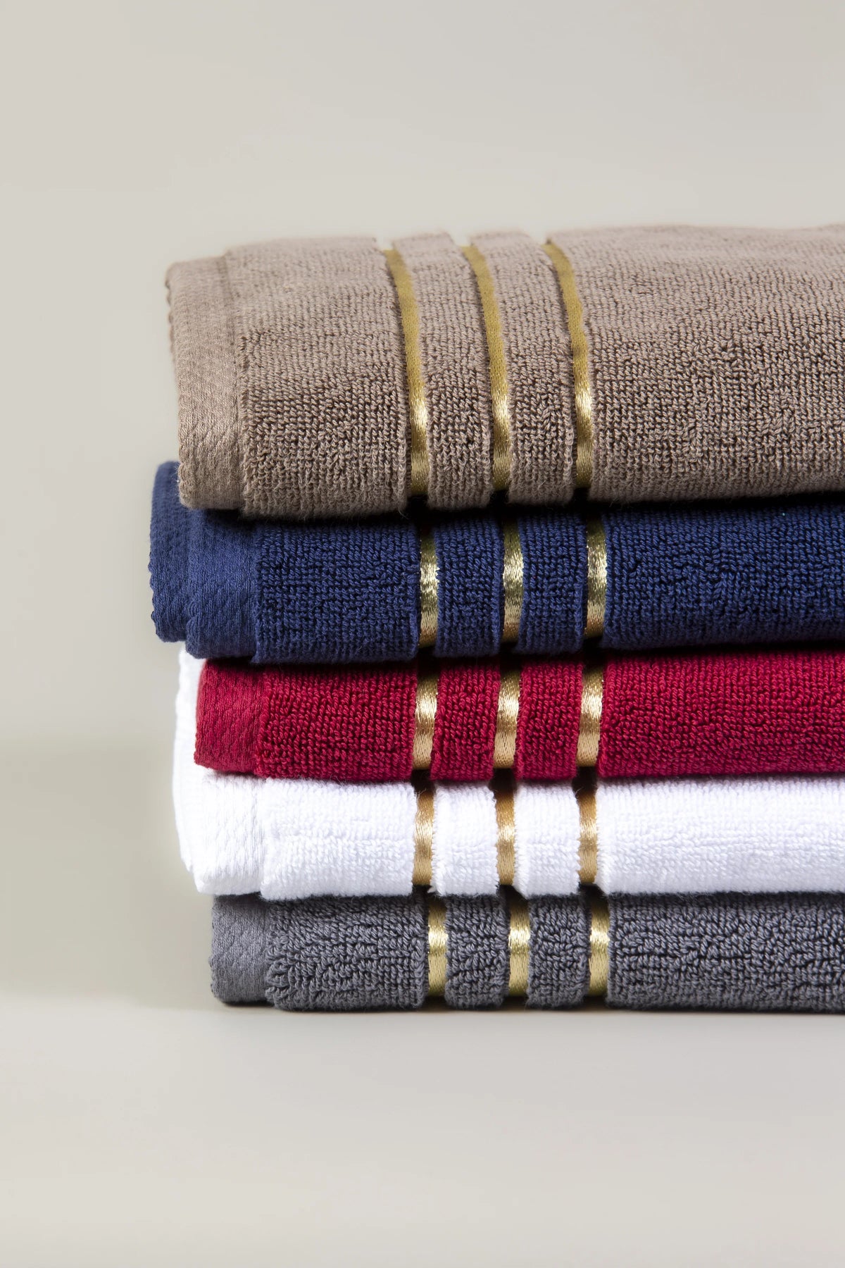 Stack of five Chateau Turkish cotton hand towels in brown, navy blue, maroon, white and grey with three gold border lines 