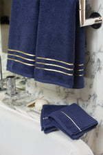 Navy Blue Chateau Turkish cotton hand towel, hanging beside a marble bathtub 