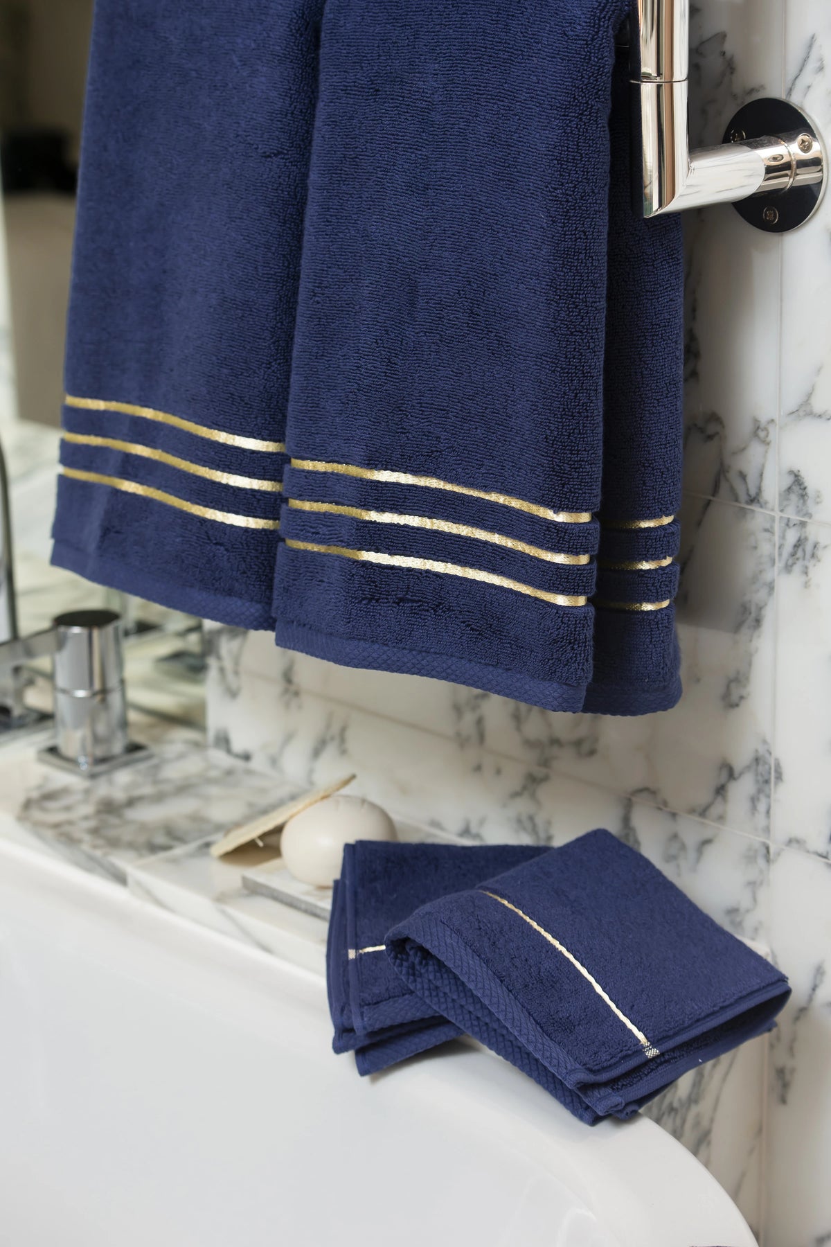 Navy Blue Chateau Turkish cotton hand towel, hanging beside a marble bathtub 