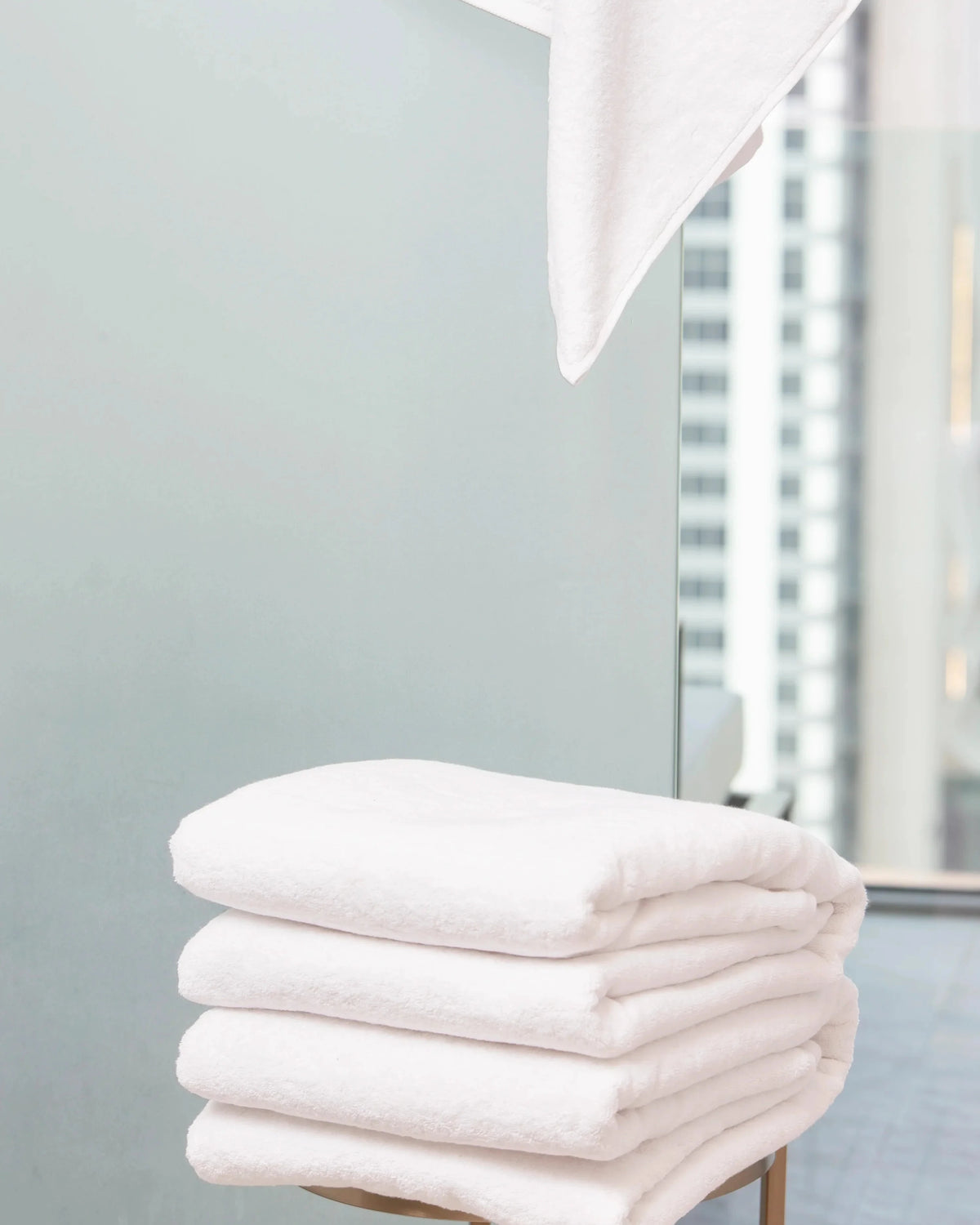 Retreat Duo Set white cotton bath towels folded on a stool by a bright bathroom window