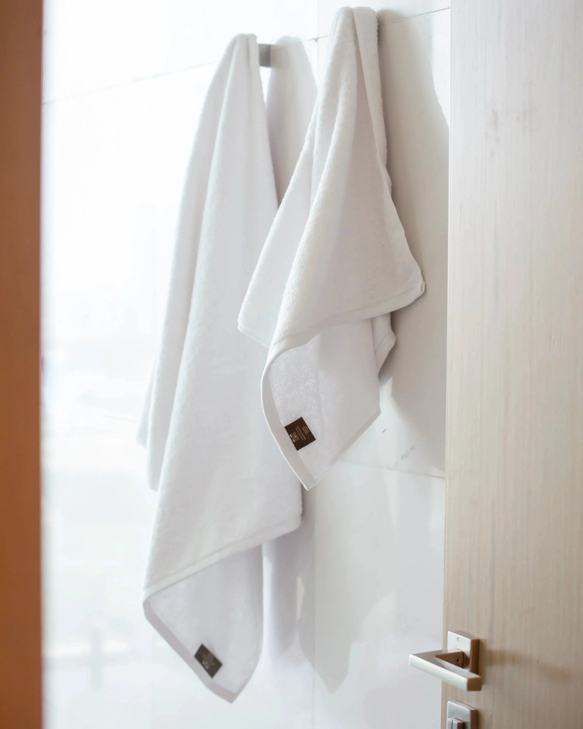 Two white Retreat cotton towels hanging on hooks in a modern bathroom