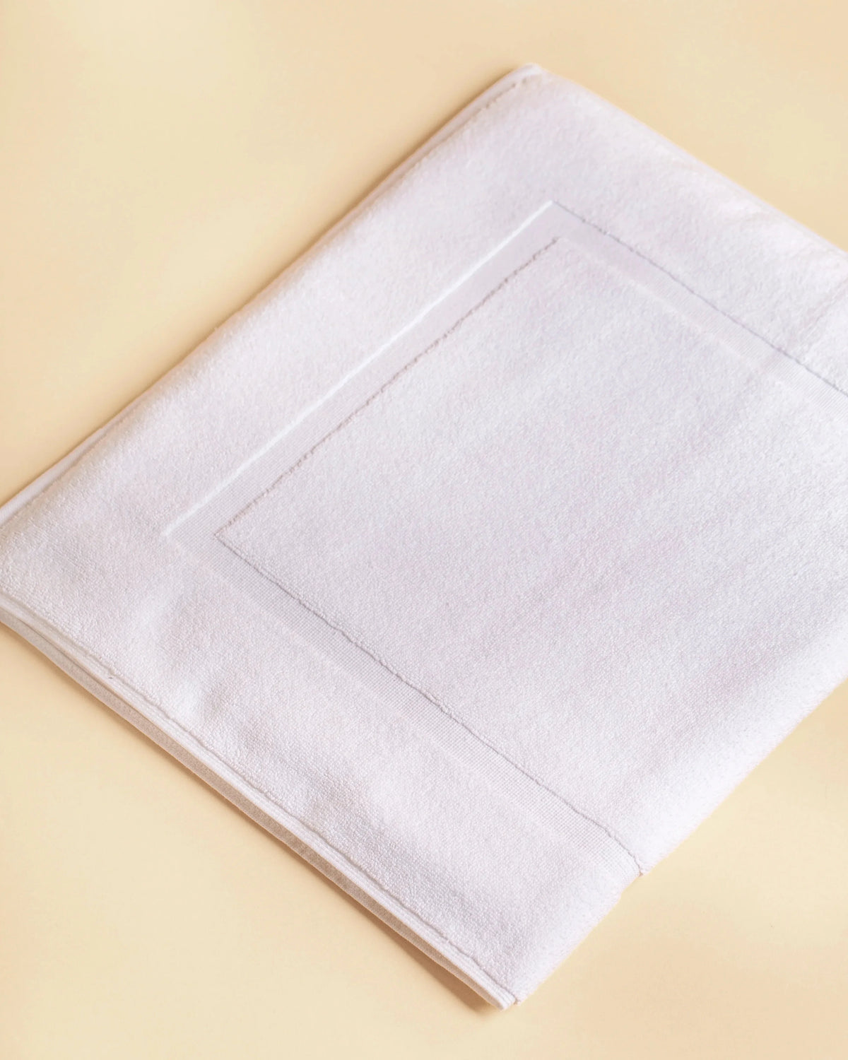 Retreat white cotton bath mat folded flat, showing the woven frame border