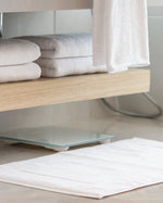 Retreat Essentials Set white towels on a vanity shelf with the bath mat on the floor
