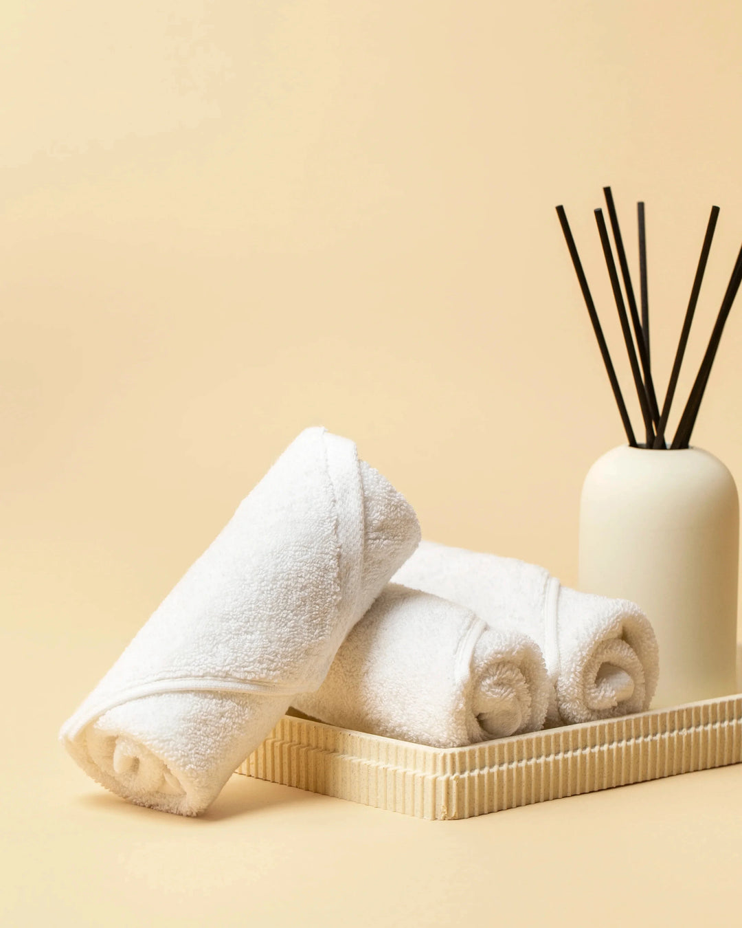 Retreat white cotton face towels rolled in a tray beside a reed diffuser