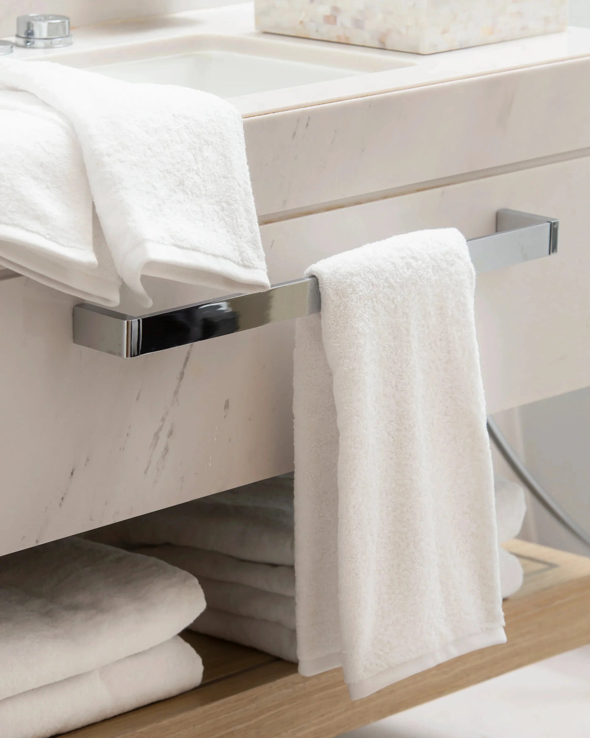 Retreat white cotton hand towel on a chrome towel rail in a marble bathroom