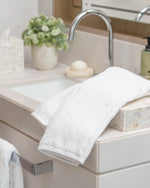 Retreat white cotton hand towel folded on a marble washbasin beside a chrome tap